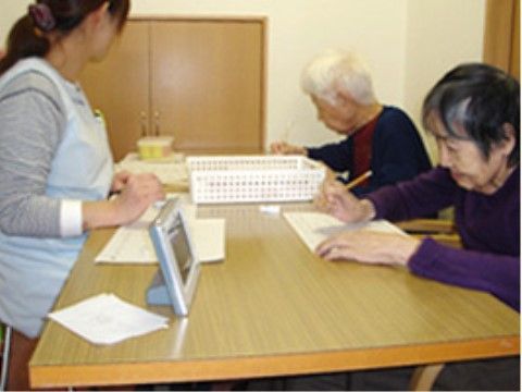 くもん式の学習に励む高齢者と見守るスタッフ