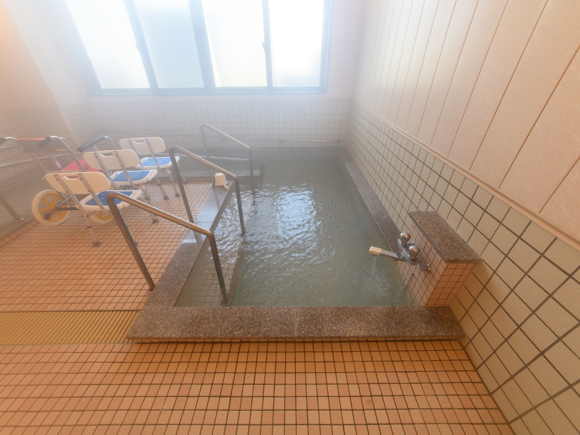 共同浴室には大きな窓があり明るい。浴槽にはスロープ、手すりを設置しており安全に入浴することができる。