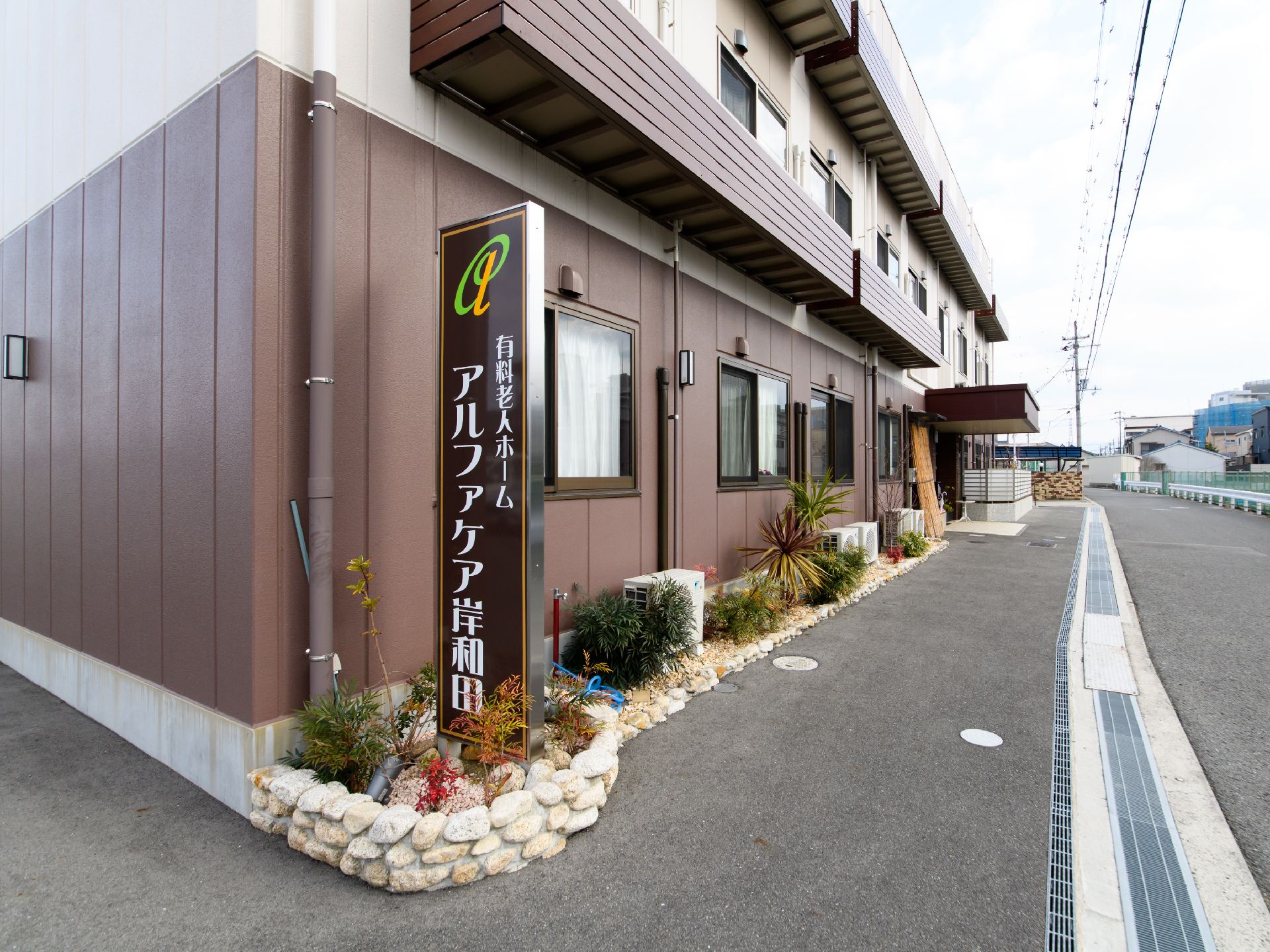 背の低い石垣の花壇に、多種多様な植物が植えられたエントランス