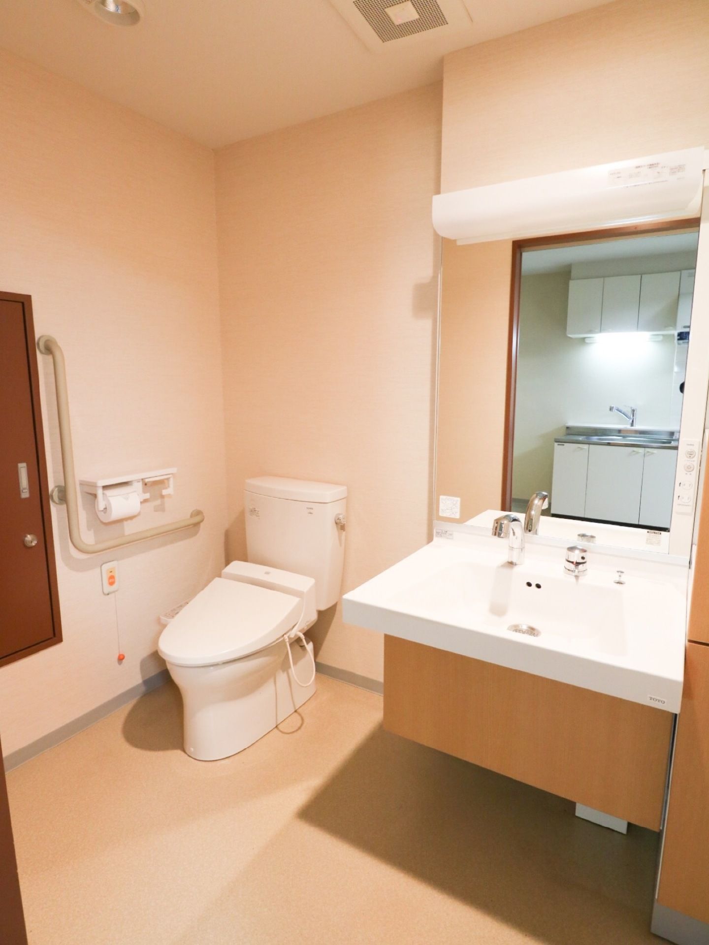 トイレは、全面が白色で統一されたデザインの室内で、温水洗浄便座仕様で右手側に手すりがある。また、便座の横には大きな洗面台がある。