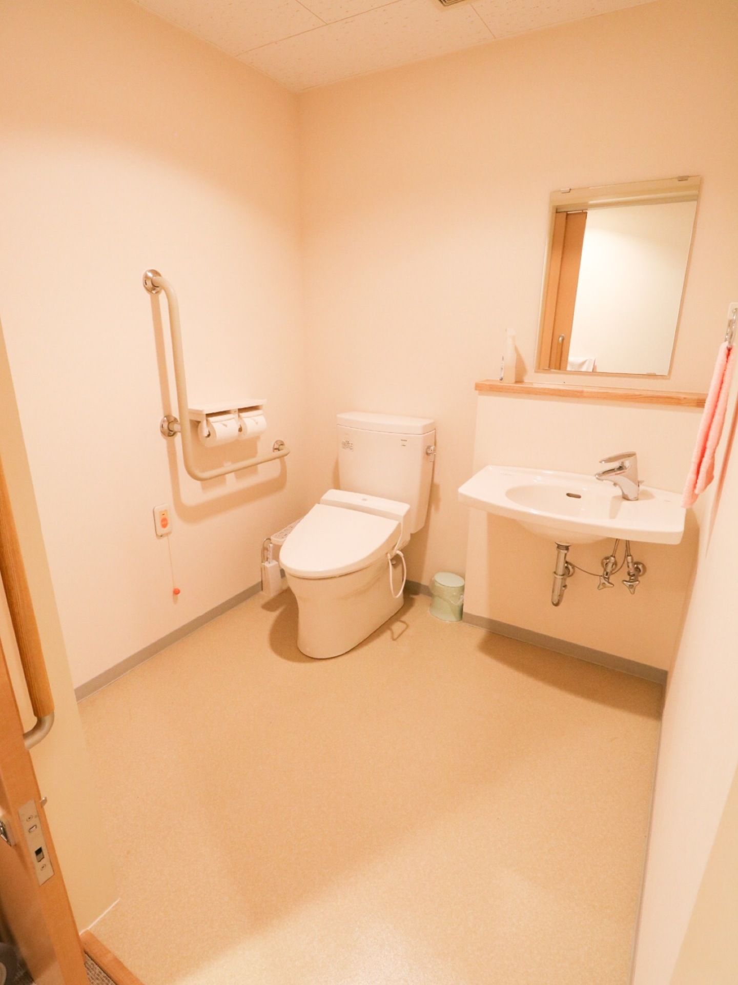 トイレは、全面が淡いピンク色で統一されたデザインの広い室内。温水洗浄便座仕様で右手側に手すりがある。