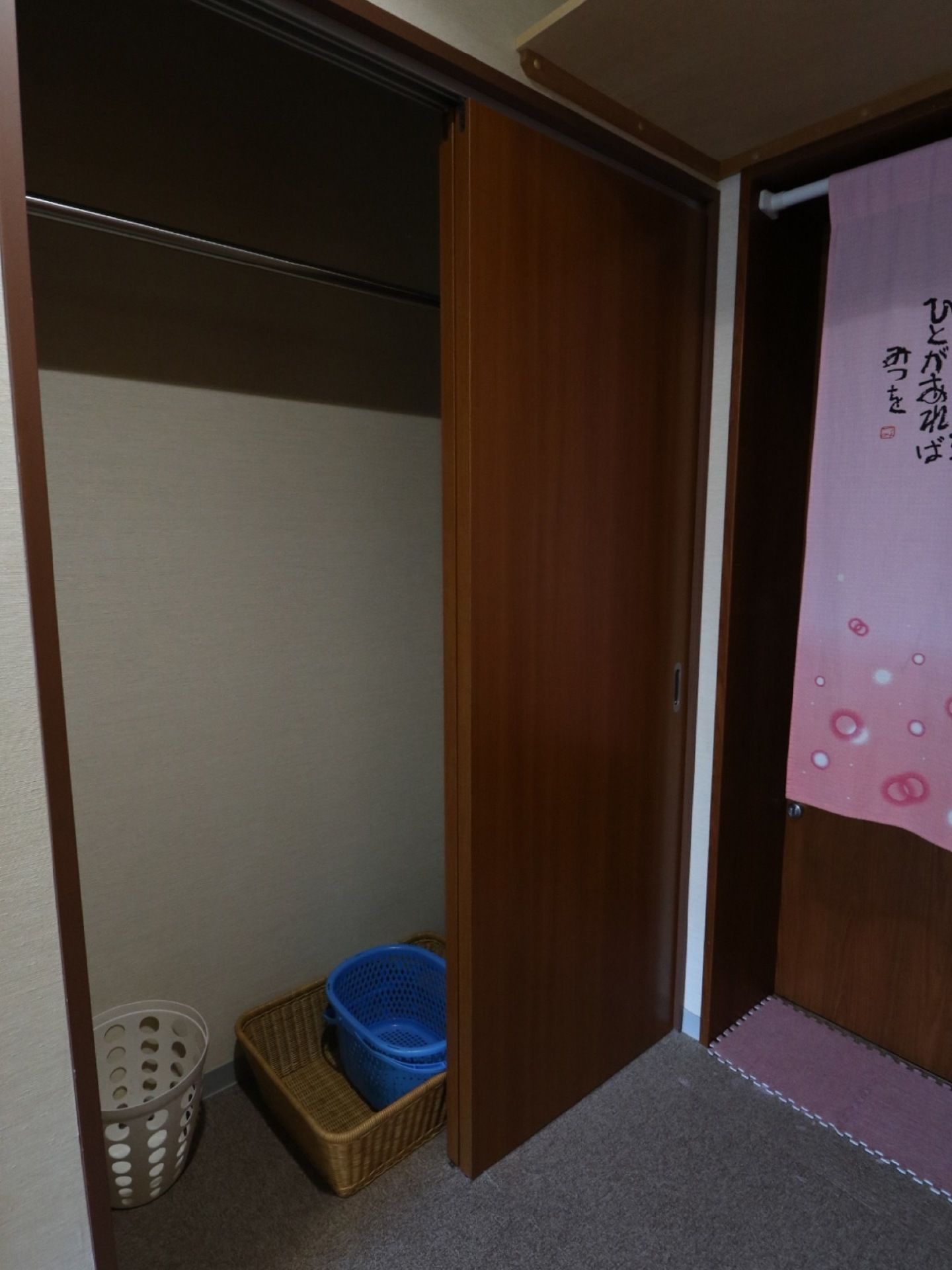 ドアの前には詩が書かれたピンク色ののれんが掛かっている。収納スペースがあり、その中に脱衣かごが置かれている。