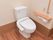 ベージュの壁と木目調のフローリングが落ち着いた雰囲気のトイレ。トイレ内には緊急通報装置が取り付けられている。