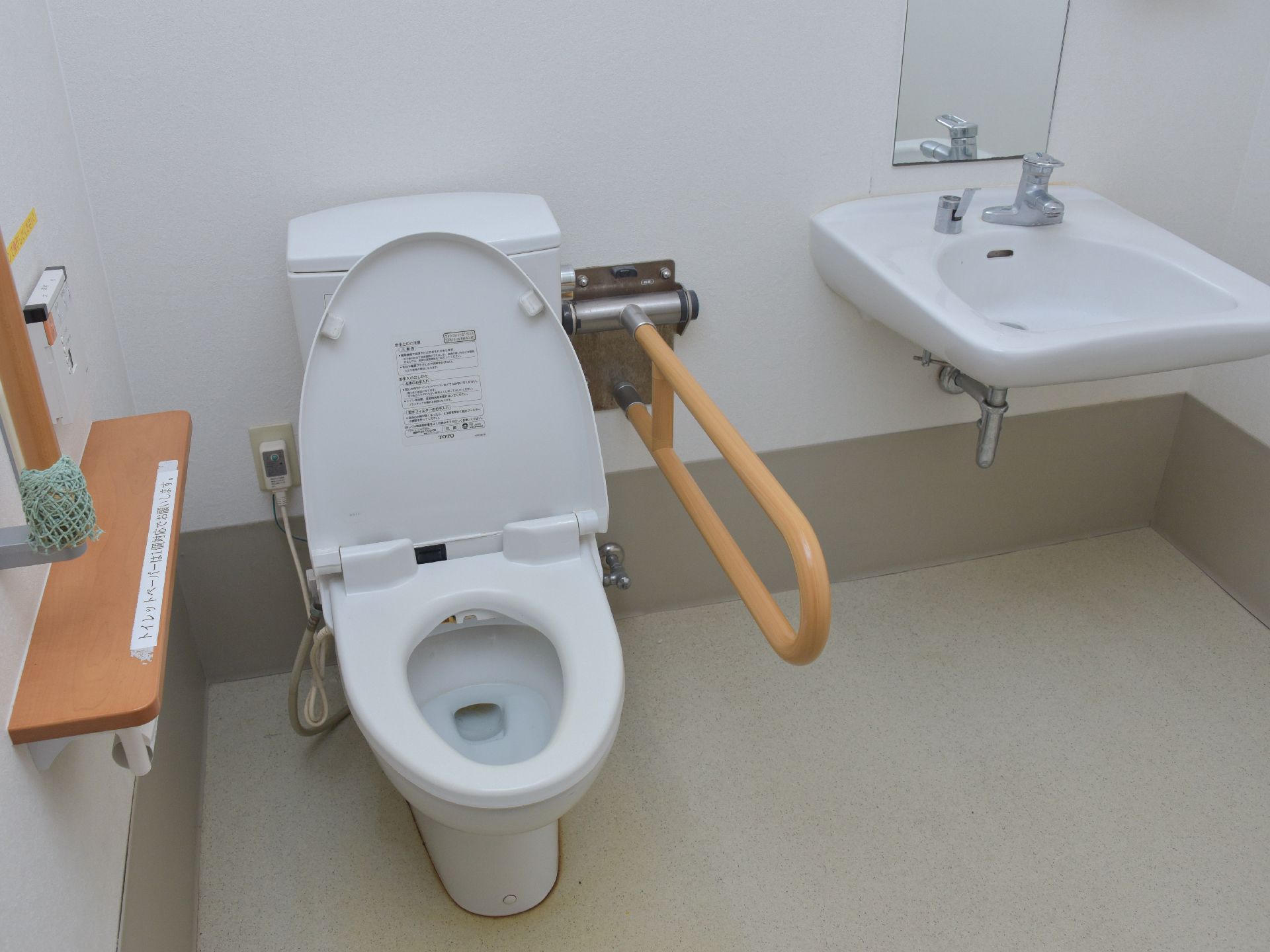トイレと洗面所が1つの空間にある。洗面台には縦長の鏡が設置されていて、トイレの両側には縦型と横型の手すりが取り付けられている。