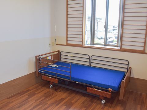 フローリングの床と薄い黄色と白の壁がある個室には青いマットで茶色いフレームのベッドが置かれている。部屋には出窓もある。
