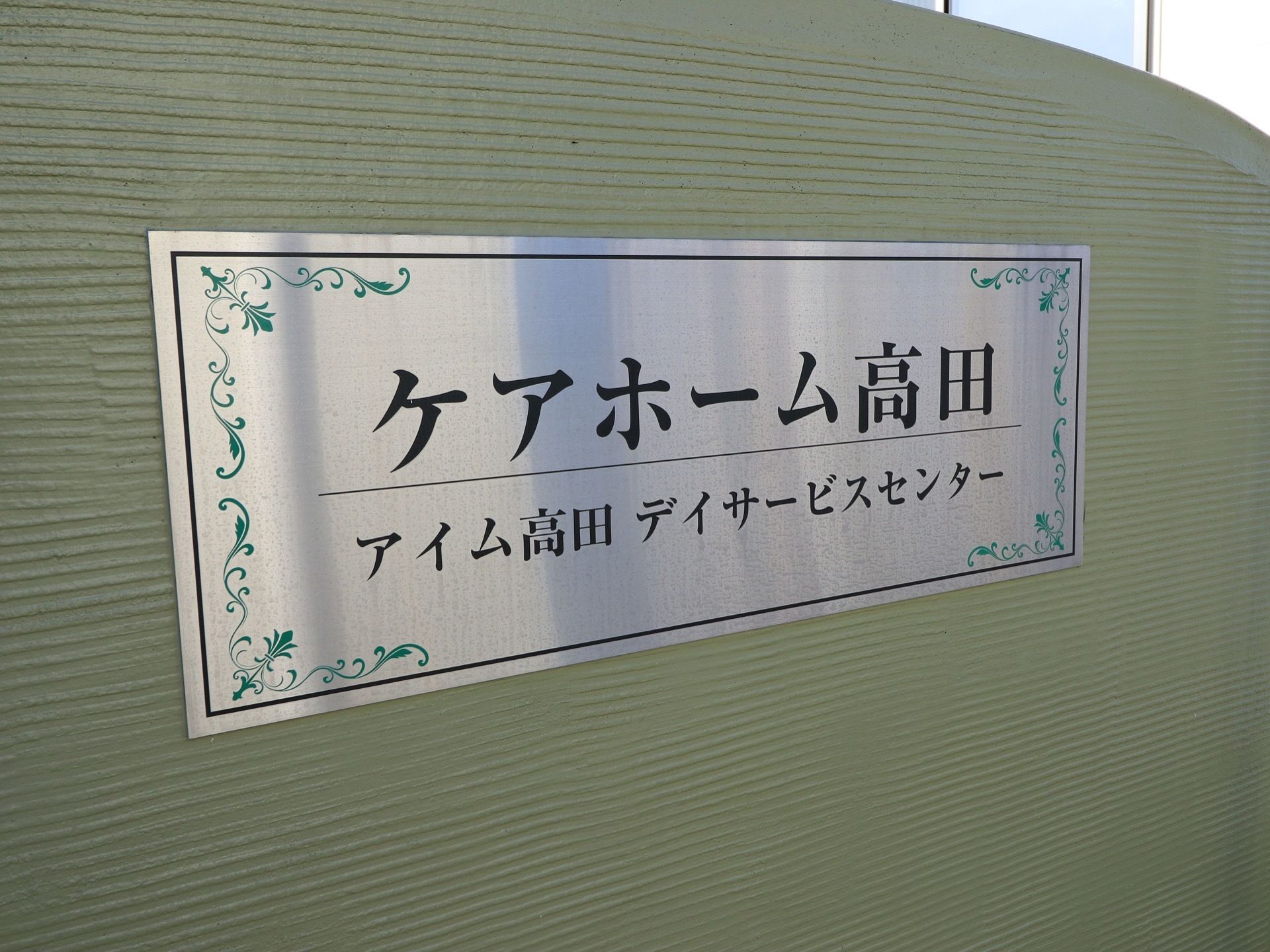 ステンレスのプレートに施設の名称が印字されている。緑色の植物のデザインと相まって、品格のある雰囲気を醸し出している。