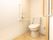 居室内のトイレは温水洗浄便座を取りつけている。壁にトイレットペーパーがあり、L字型の手すりと非常ボタンが設置されている。