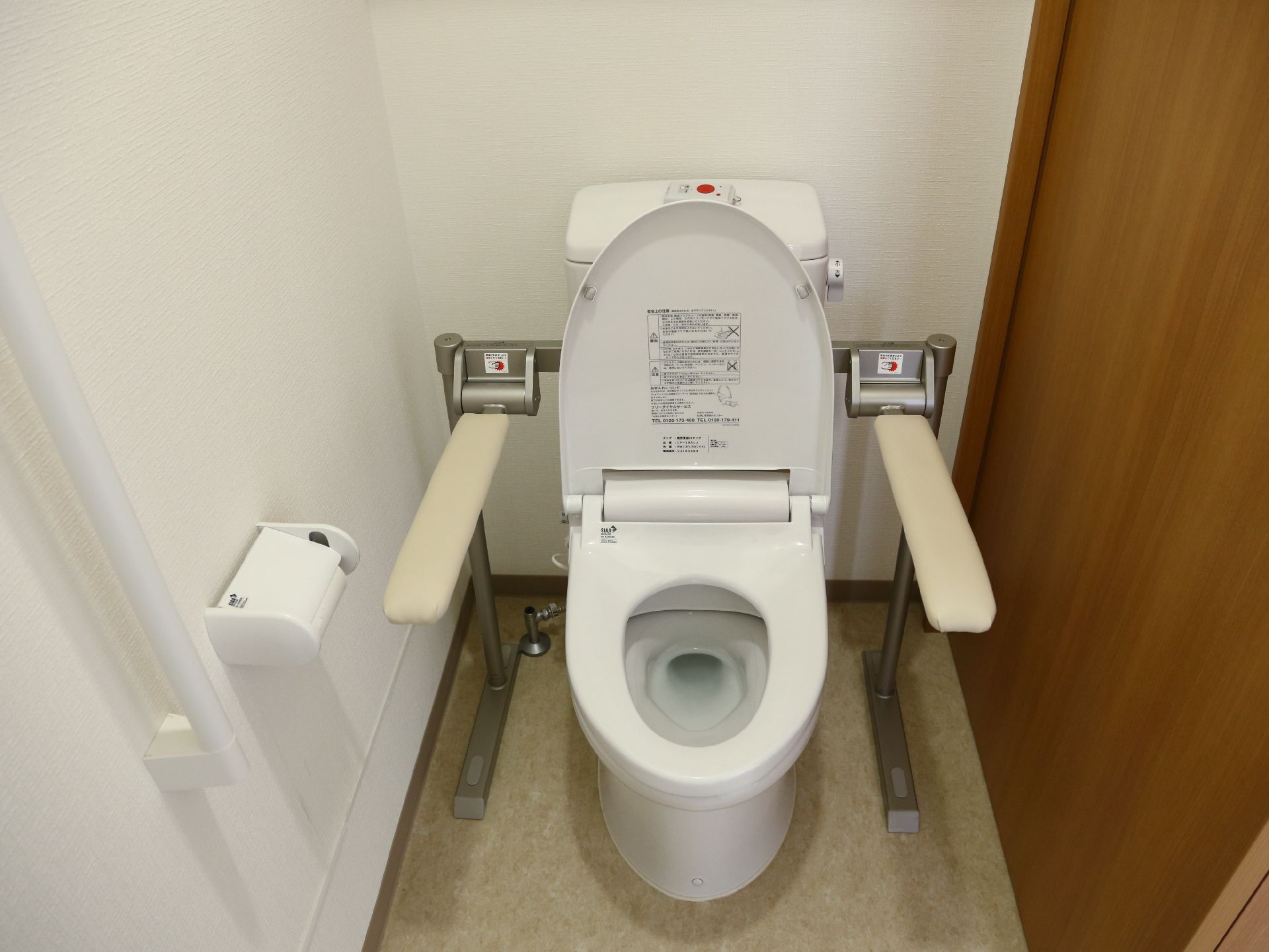 スライド式の木目調扉を採用したトイレ。ベージュの床に白い壁。足腰の不自由な方にも安心して使える手すり付き。
