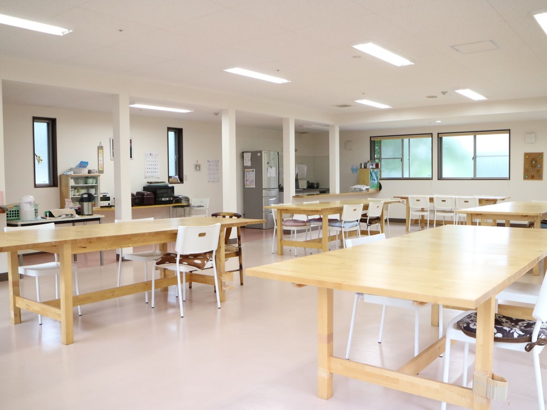 フロア隅にキッチンが配置されている、開放的な食堂である。複数の木製のテーブルと白い椅子が配置されている。