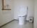 白を基調とした清潔感のある個室トイレで、壁にはＬ字型の手すりや呼び出しボタン、ペーパーホルダーがかかっている。