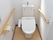 白い壁とベージュの床が明るく清潔感のあるトイレ。ウォシュレット付きトイレには、手すり、緊急通報装置が設置されている。
