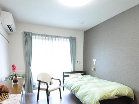 居室の壁際にはベッドが置かれている。１人掛け用の椅子が用意されている。チェストの上には浴物が飾られている。