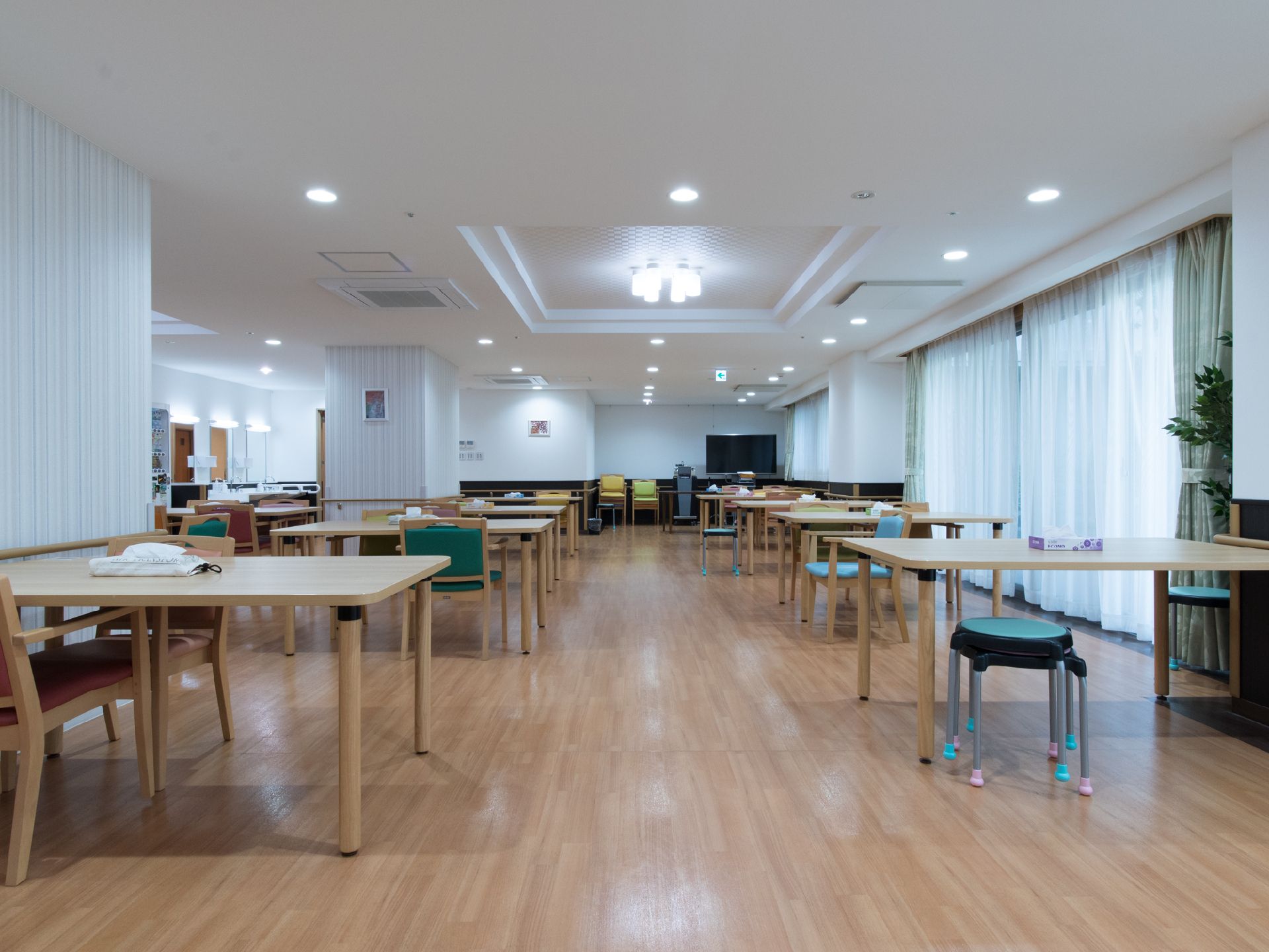 施設利用者が集まれる部屋である。通路は車いすでも通行ができる程の幅がある。テーブルや椅子は空間にゆとりをもって置かれている。