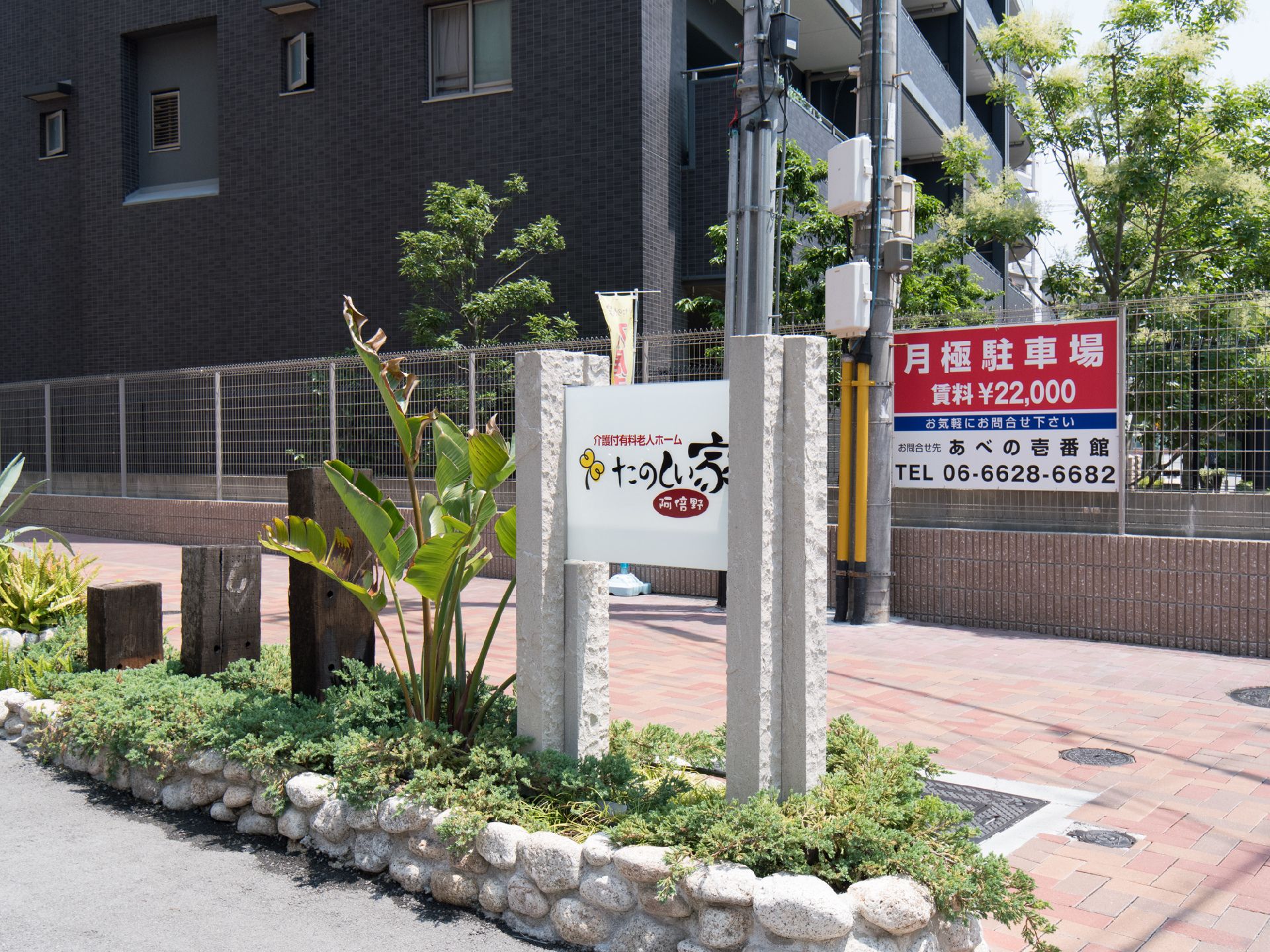 屋外で施設の所在を表す看板。重厚な石が植え込みの中に立つそれは、ただの商業看板と言うよりもはや現代美術に近い。