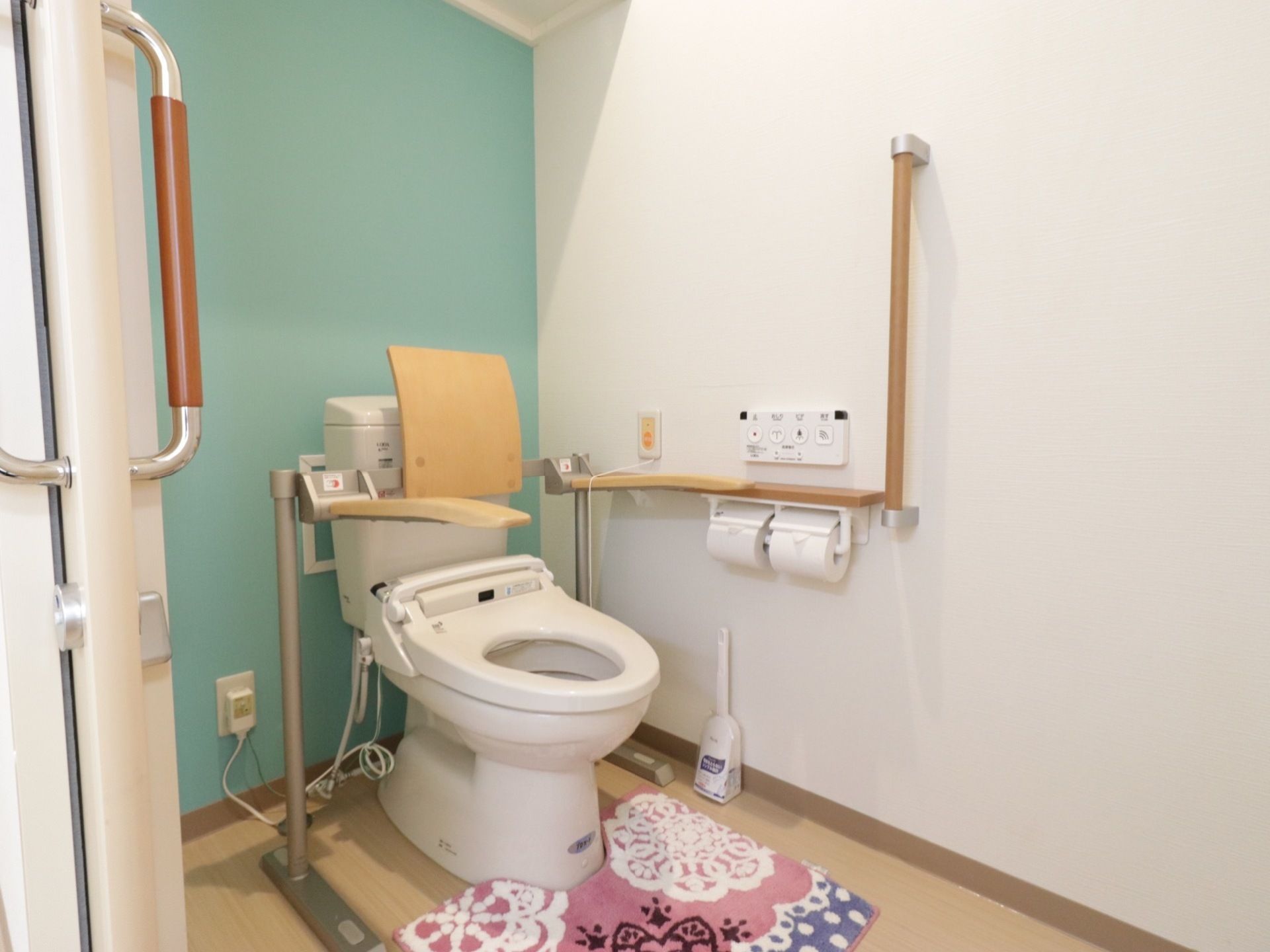 トイレの壁には手すりや緊急時コールボタン、便器の両側には肘置き、背もたれ、温水洗浄便座と快適に利用できる。