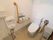 便座が中央にあるトイレルームは、両サイドに木製の手すりがあり、壁際にはトイレットペーパーやゴミ箱がある。