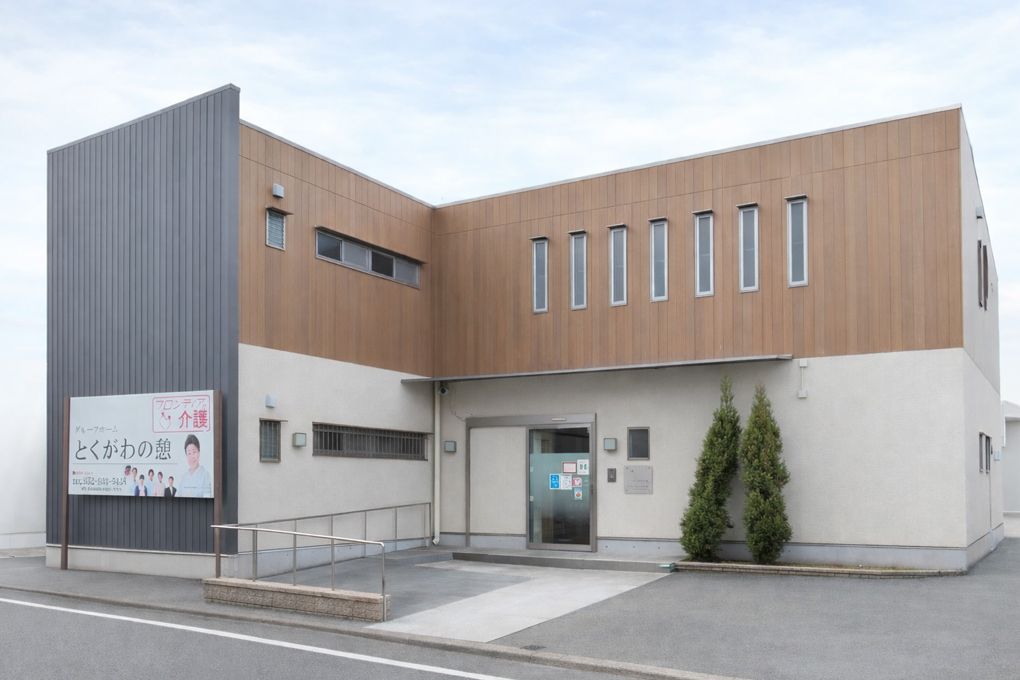 2階建てとなっている施設はL字型の建物となっている。左手には大きめの看板があり、施設名と人の写真を見ることができる。