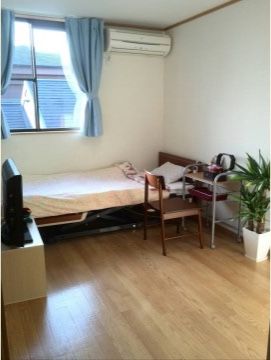 リフト付きのベッドが置かれた居室。大きめの窓からは自然光が入り明るい。机と椅子の横には観葉植物も置かれていてオシャレな雰囲気だ。