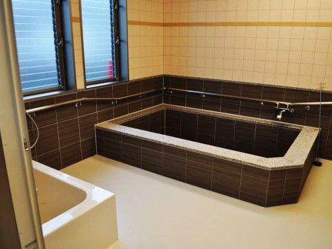 ゆったりとくつろげる大きな浴槽。窓からは光が差し込み、白、茶色のタイルも明るく清潔である。手すりも設置されている。