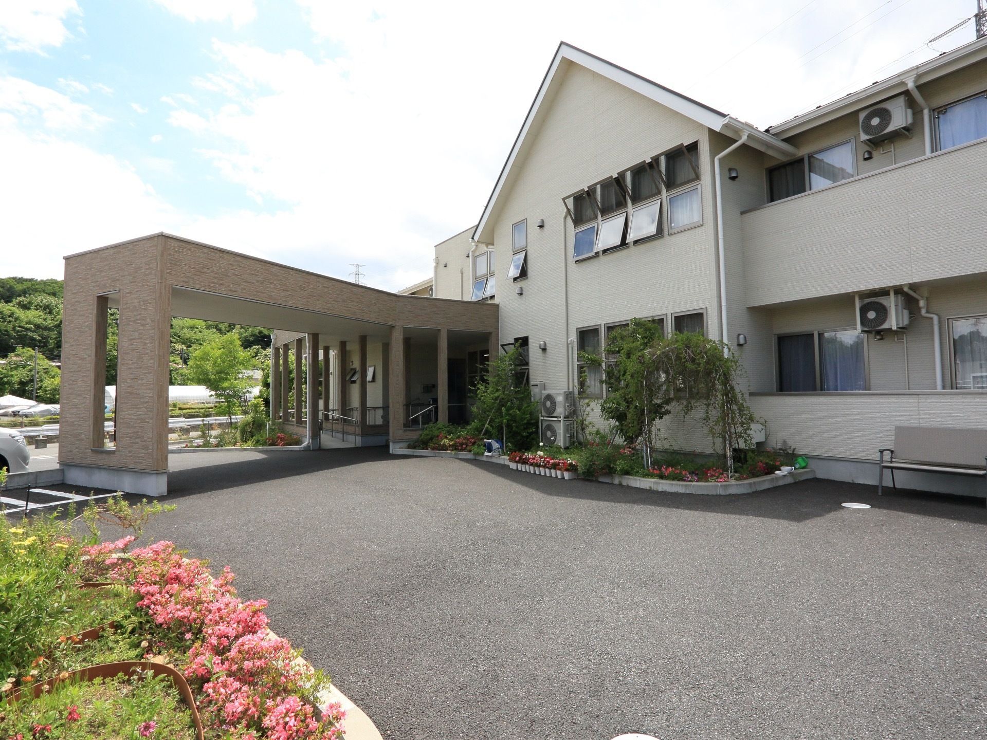 豊かな自然に囲まれたグループホームである。屋根付きの玄関となっており、施設目の前はアスファルトで舗装されている。