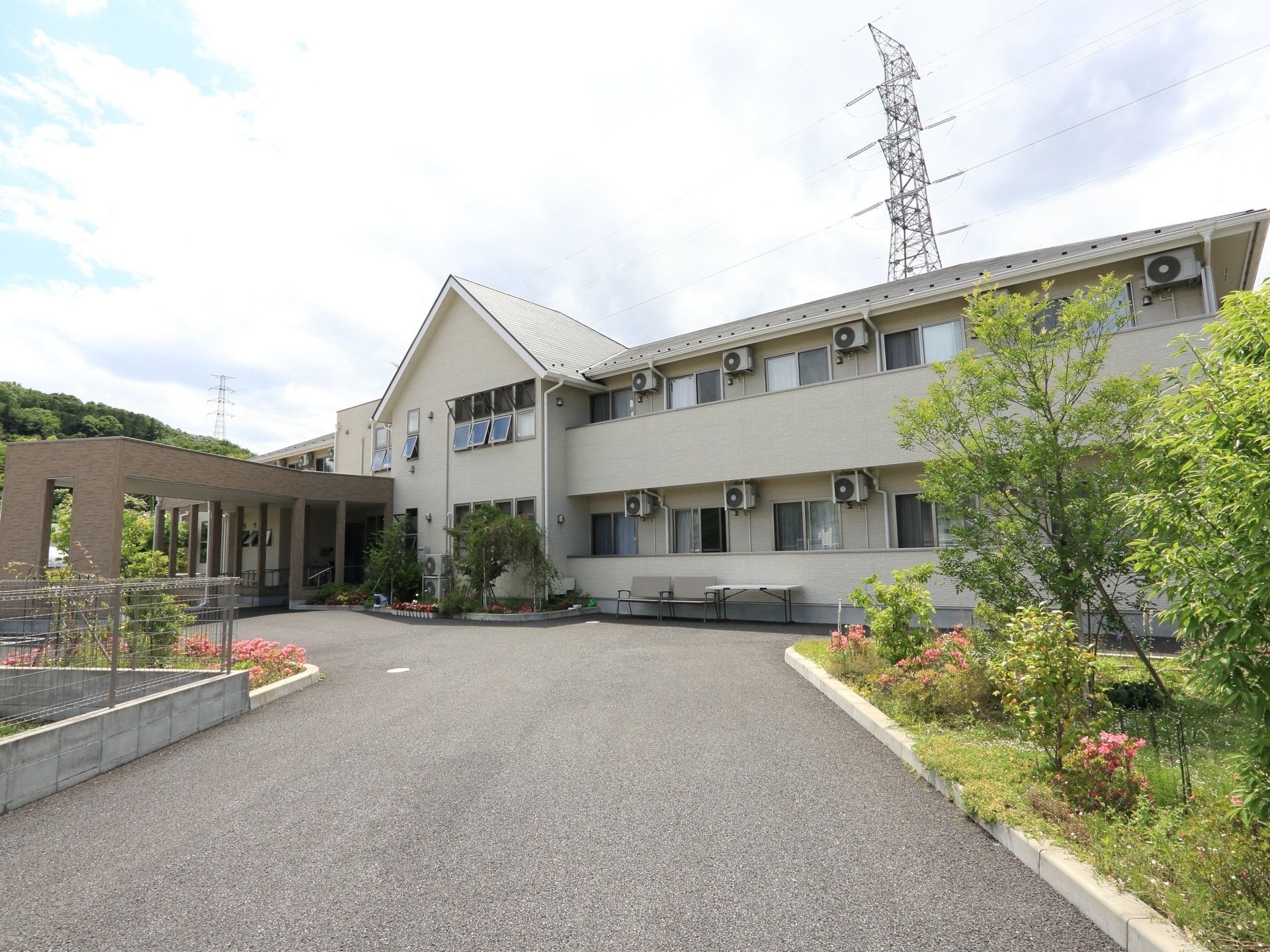 広い面積を有した白を基調としたグループホーム。外壁沿いにベンチが置かれており、各部屋にはベランダが設置されている。