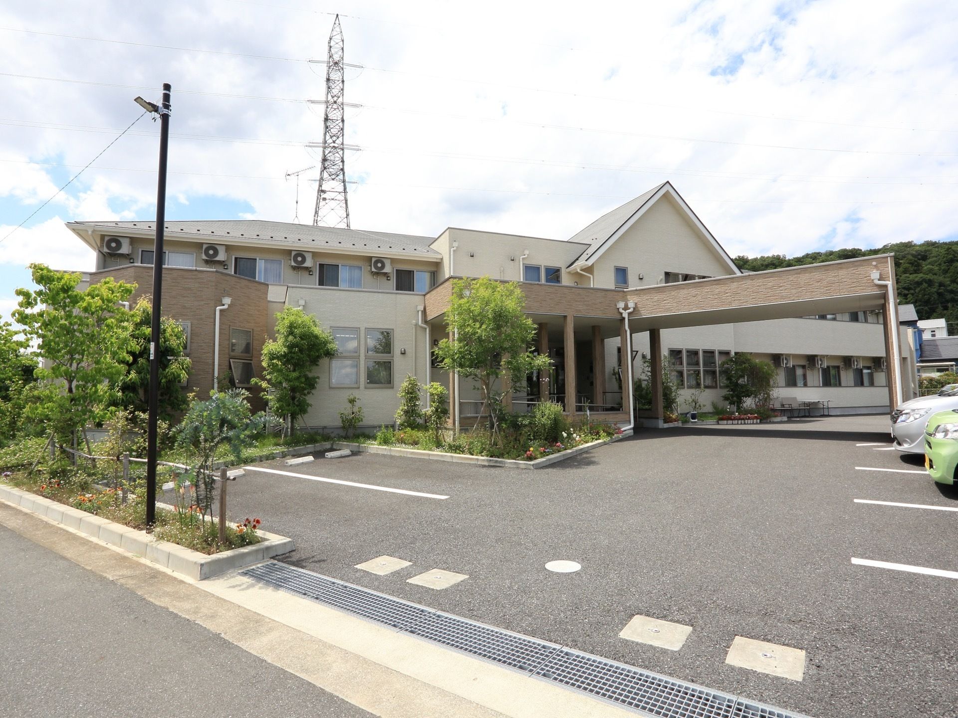 敷地内にアスファルトで舗装された広い駐車場があり、車が複数停められている。道路沿いに花壇が設置されている。
