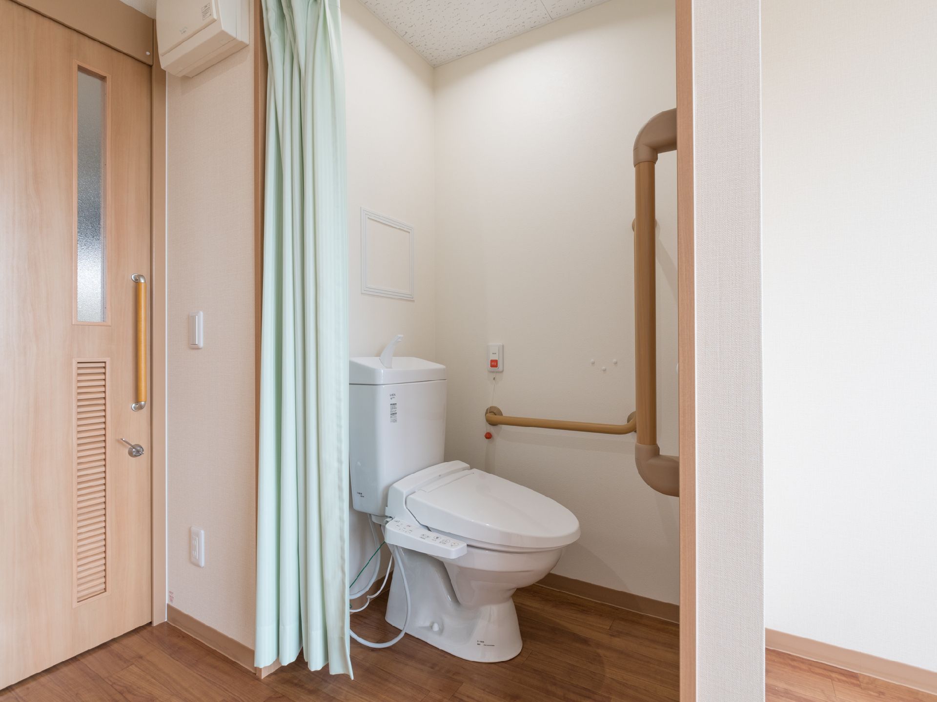 個室入り口すぐには薄い水色のカーテンが掛かったトイレがある。トイレを入ってすぐと奥の壁側には手すりが取り付けられている。