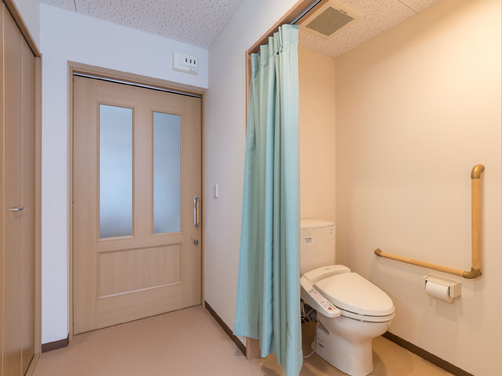 個室にはトイレが設置されている。トイレには扉がなく、薄い緑色のカーテンで仕切られている。トイレの壁側にはL字型の手すりが付けられている。