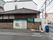 瓦屋根のある建物の前には塀がある。塀には大きな施設の看板がある。隣には近くの診療所の看板も貼られている。