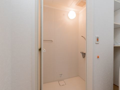 お風呂の中の壁の上部には丸い照明が取り付けられている。タオルハンガーやシャワーもある。外には呼び出しボタンが設置されている。