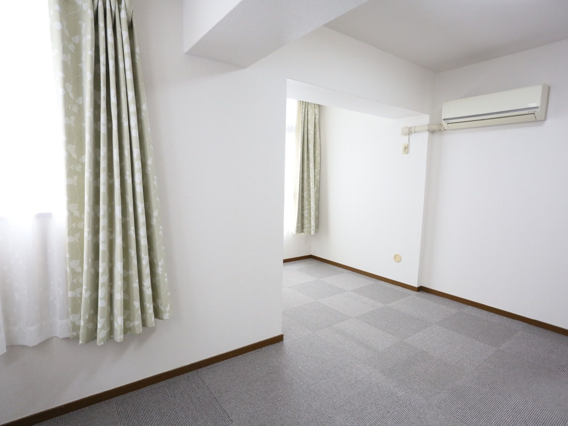 室内のそれぞれの窓には、模様付きの淡い色合いのカーテンが留められている。天井近くの一角には、エアコンが取り付けられている。
