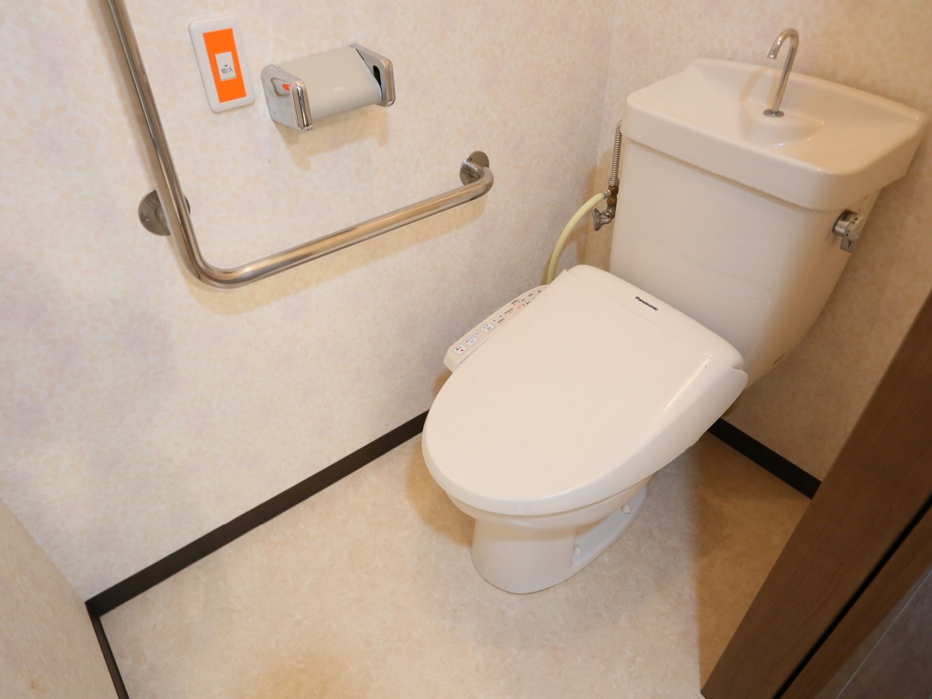 淡く模様の付いた壁や床面に囲まれた明るい雰囲気のトイレである。便器横の壁には手すりやつかまり用の棒が備え付けられている。