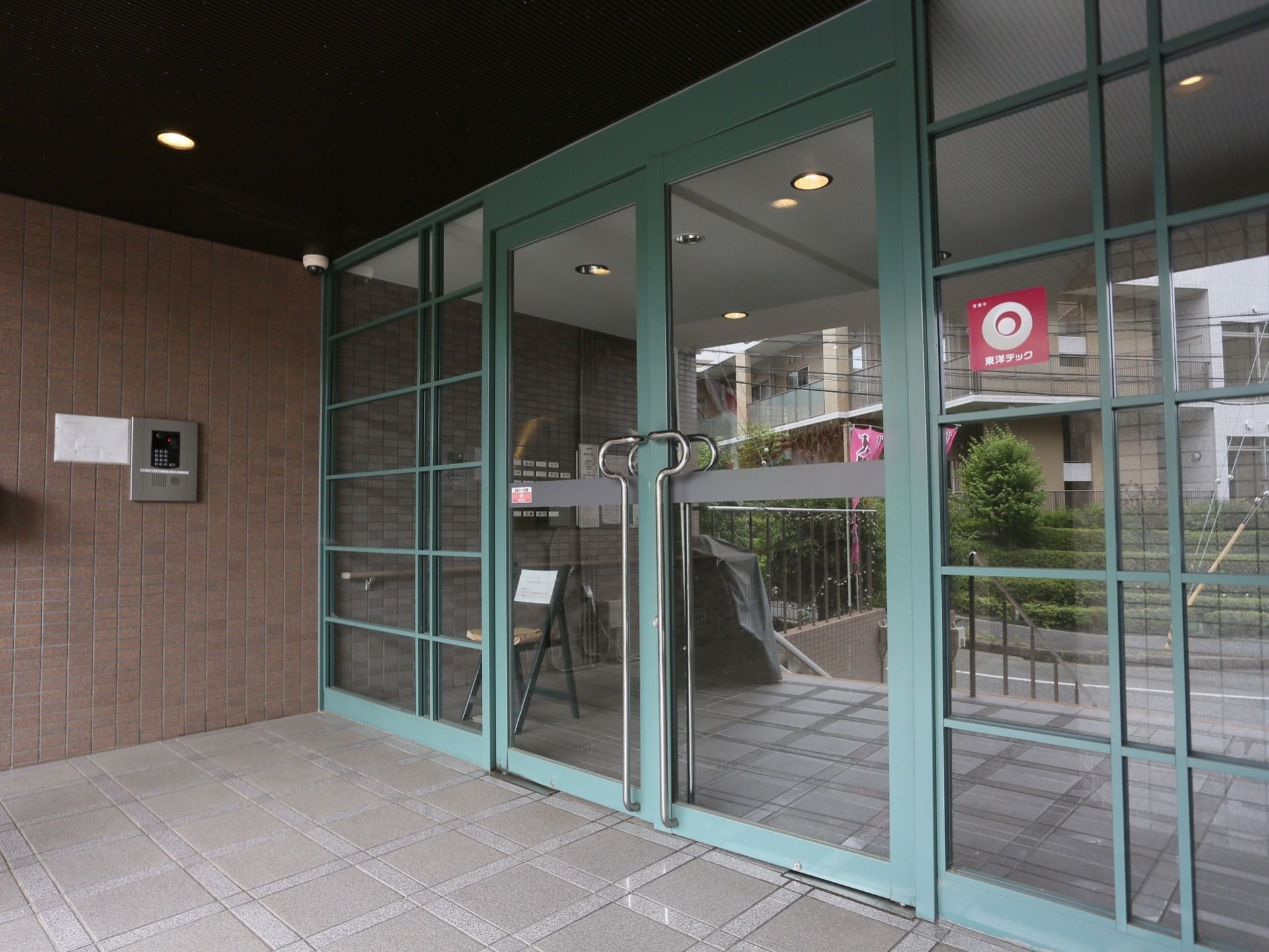 施設の玄関は、玄関扉と両脇の壁面がガラス張りになっておりモスグリーンの枠が付いている。扉の脇には石造りの壁面にインターホンが設置されている。