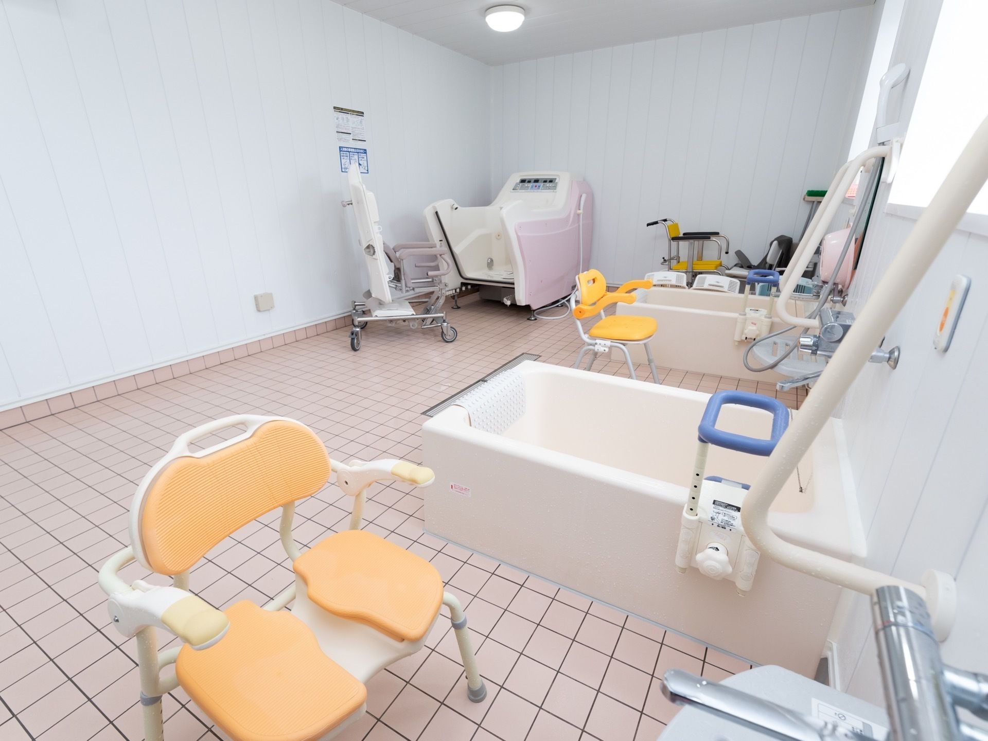 大浴室の左奥に、介護用入浴機器が備え付けられている。車椅子の部分が外してあり、浴槽の中が見える状態になっている。