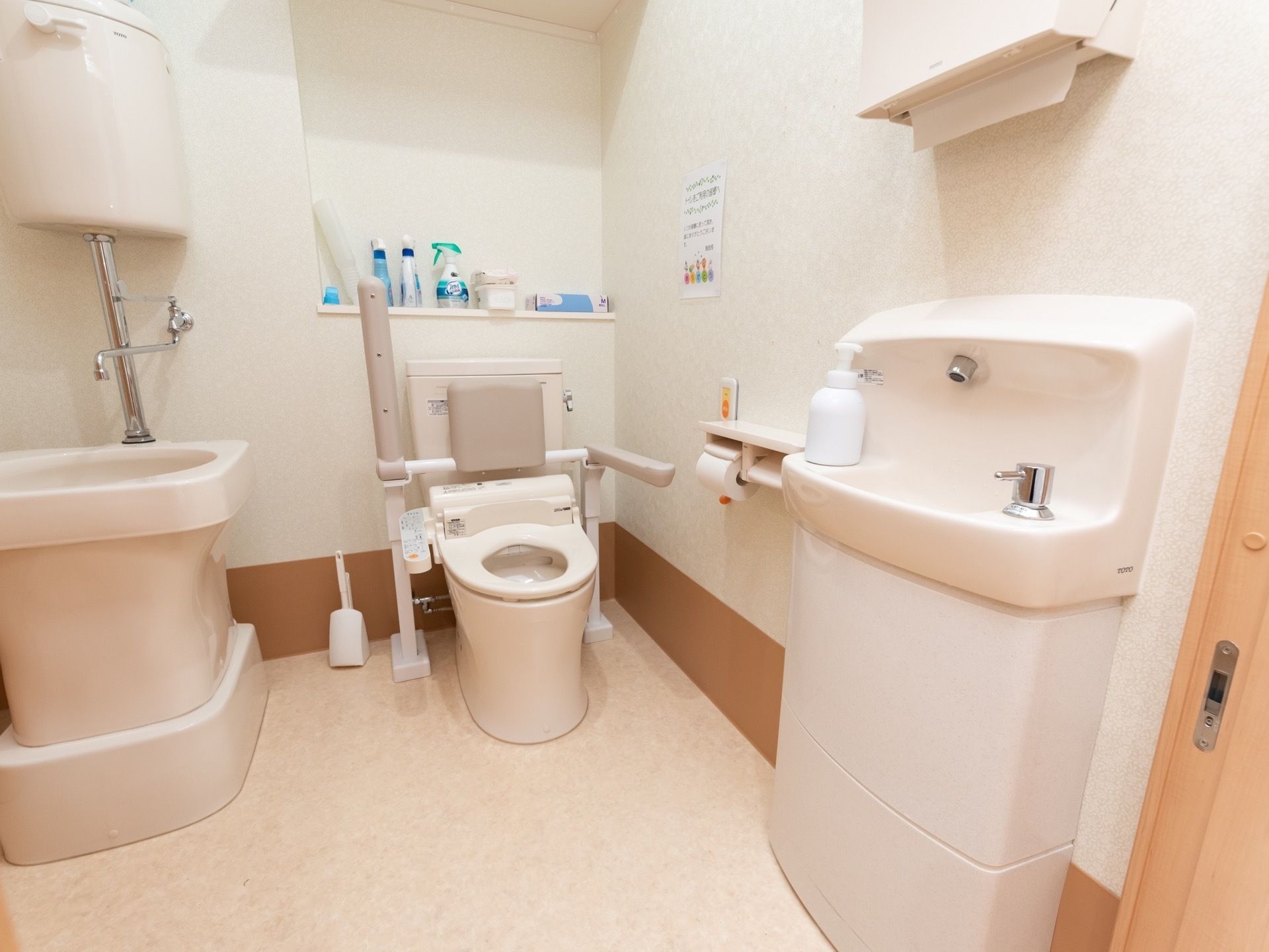 広々としたスペースが確保された共用トイレである。フタがないタイプのトイレには、背もたれや跳ね上げ式の手すりが付いている。