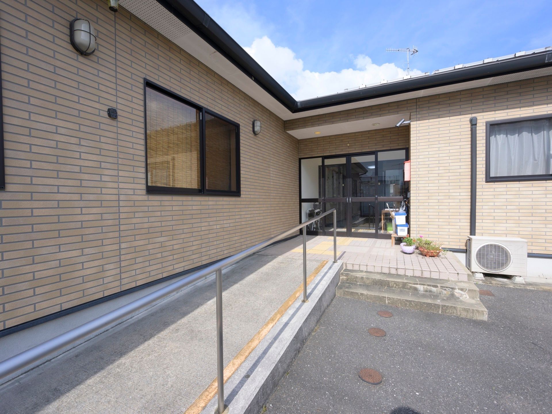 Ｌ字型をした平屋建ての住宅が建っている。玄関前は、階段のほかに手すりの付いたスロープが設けられている。