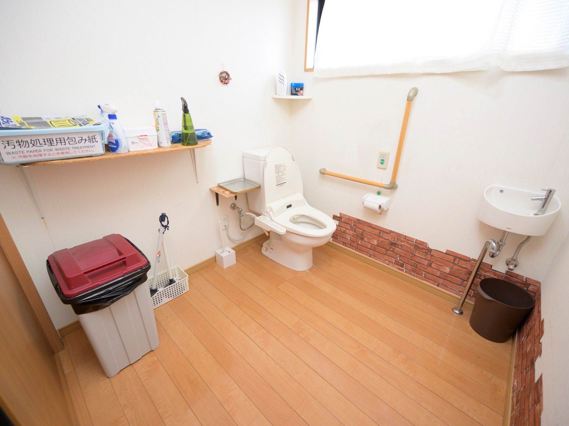 フローリングが敷かれた広いトイレがある。壁にはＬ字型の手すりが設置され、近くには緊急通報装置も付いている。