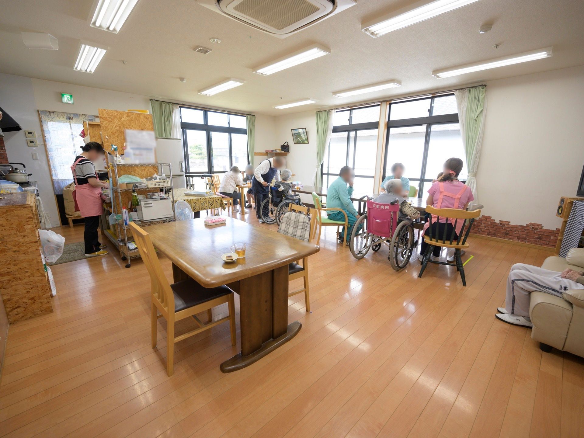 キッチンでは、スタッフが１人で作業を行っている。ダイニングテーブルでは、入居者様とスタッフが集まって談笑をしている。
