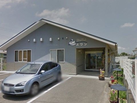 入口前のフェンス沿いに、鉢植えの花を飾っている。白いラインを引いた駐車スペースがあり、車でのアクセスも可能である。