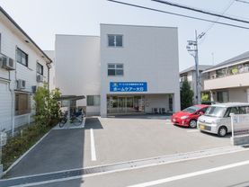 道路側には駐車場と駐輪場がある。建物の入り口はガラスの自動ドアで、入居者募集の張り紙などがされている。