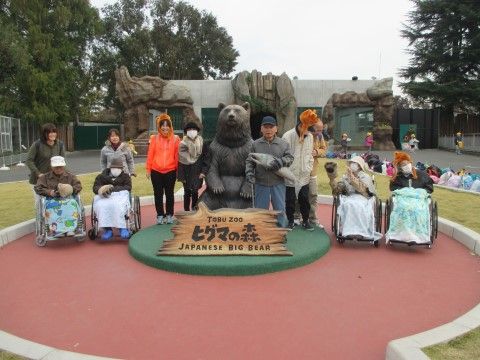大きなクマの銅像と一緒に笑顔で写る、スタッフと入居者様たち