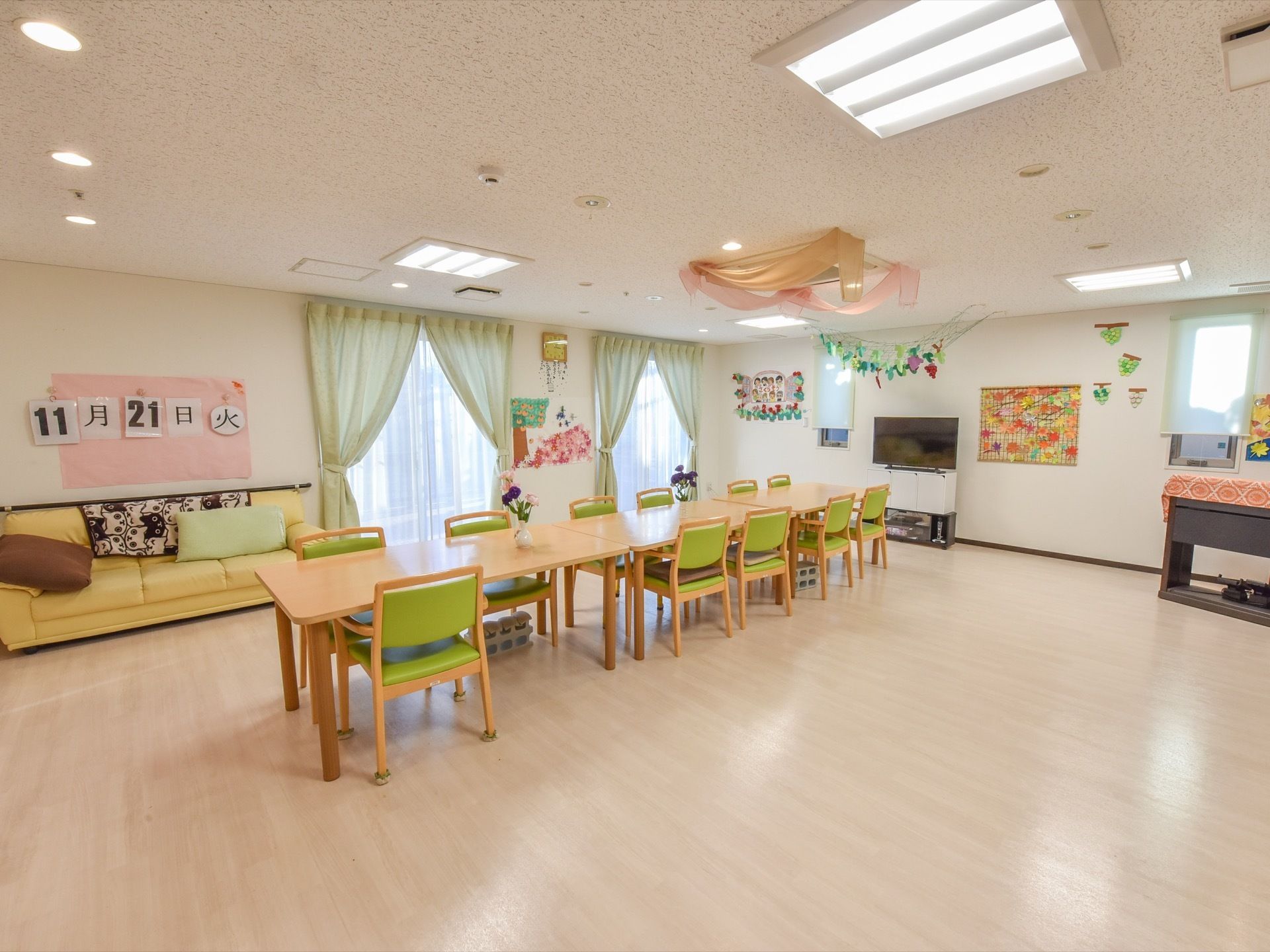 壁に手描きの作品が飾られたあたたかい雰囲気のオープンスペースは、食事時間になると入居者様が全員揃いおしゃべりをしながら楽しく過ごしている。