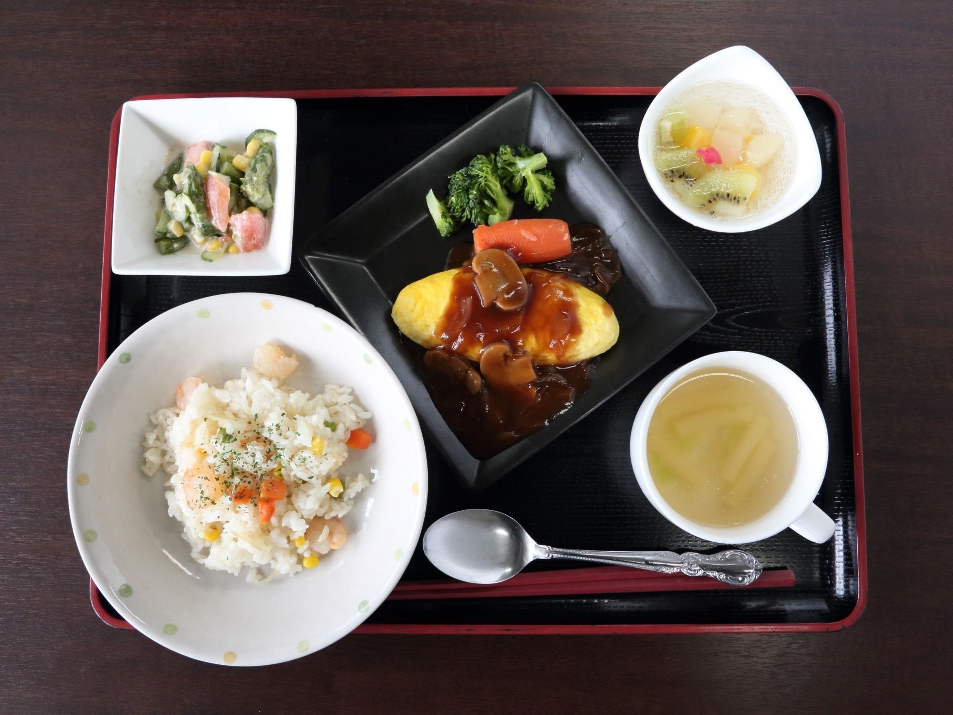 黒いお盆の上に、食事の支度がされている。この日のメニューは洋食で、デザートのフルーツも添えられている。