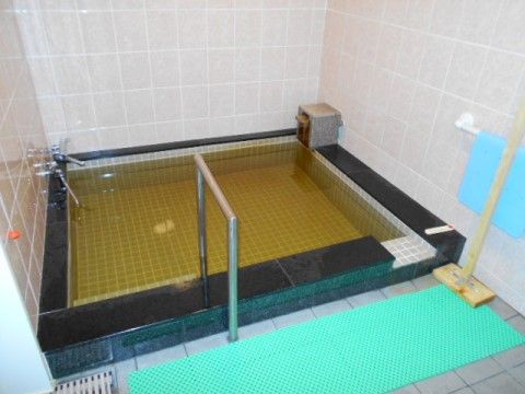 タイル張りの浴槽で、複数人が入浴できる大きさである。浴槽の手前には滑り止めマットが置かれ、手すりも設置されている。