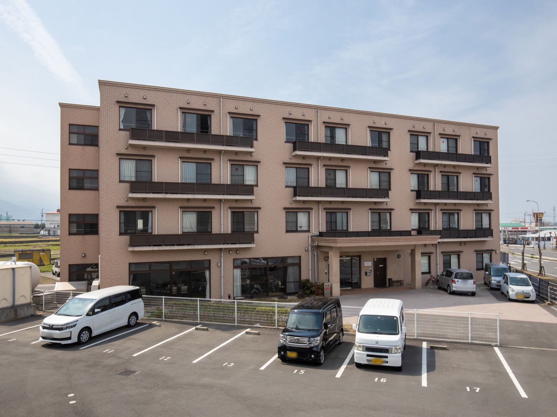ピンク色の外壁が特徴の4階建ての建物が当施設である。三角形の敷地で、建物正面には駐車スペースがある。