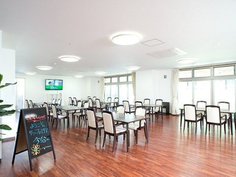 広々とした明るい空間のリビングは、開放感に溢れている。テーブルを並べ、正面にテレビを備えている。隅に観葉植物を飾っている。