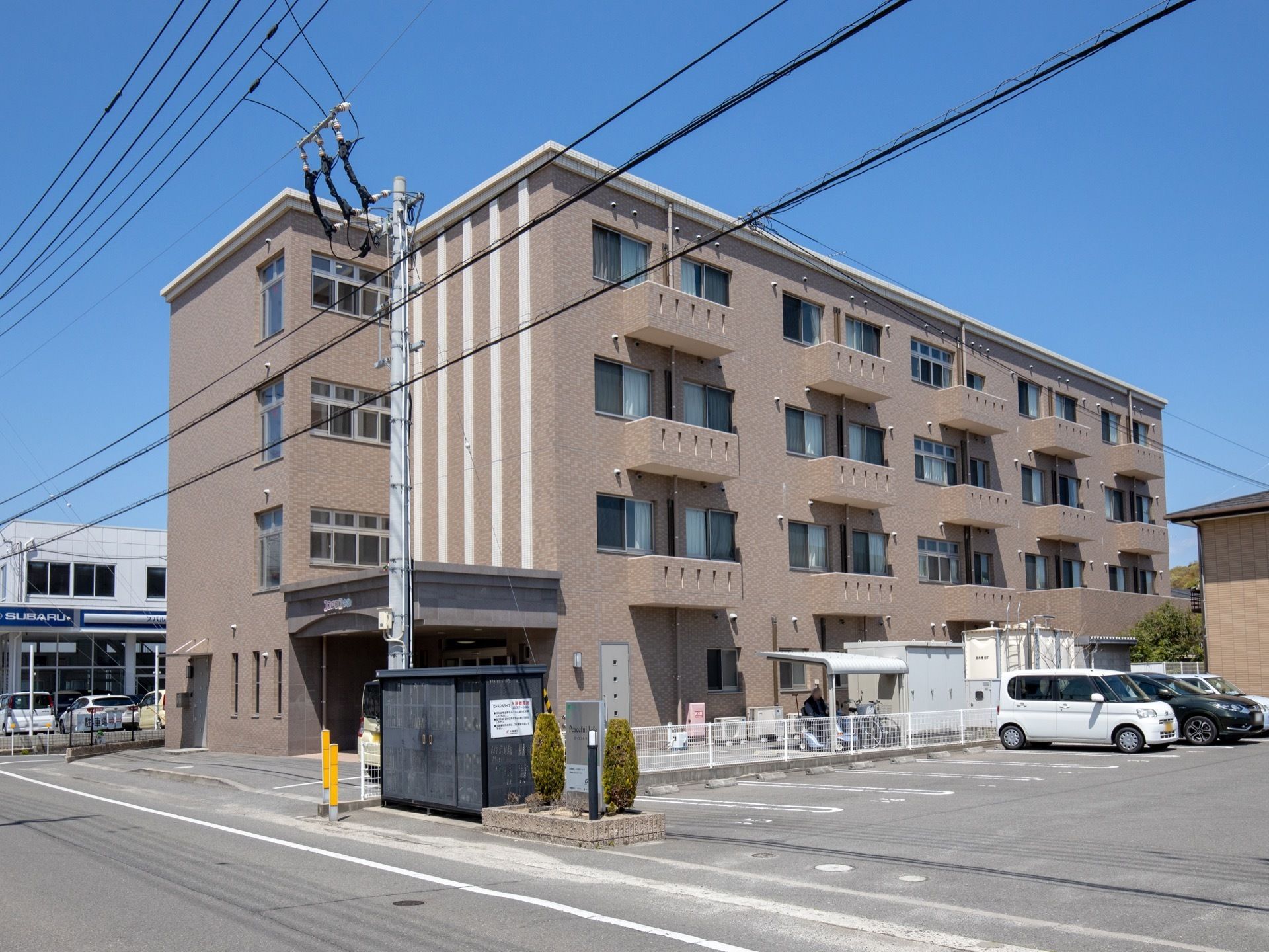 道路に面した場所に４階建ての茶色い建物がある。各部屋には窓がついていて、日当たりが良い造りになっている。