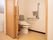 木製の引き戸がついた洋式トイレがある。段差がなく、便座の両側に手すりがついたバリアフリー設計になっている。