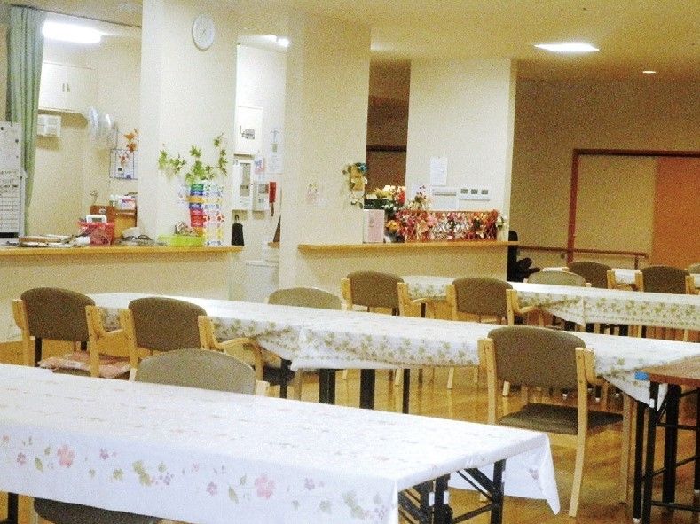 白地に花柄の模様のテーブルクロスが掛けられたテーブルが並び、背もたれと肘掛けが付いた椅子が備えられている。