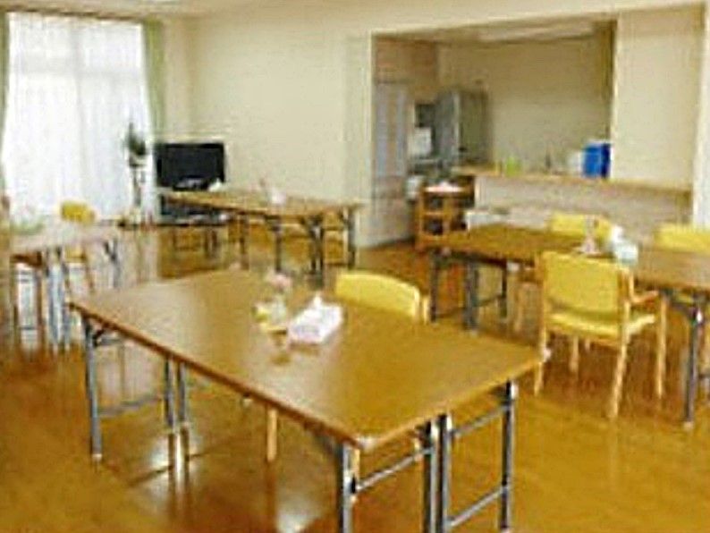 入居者様がテレビを観る部屋は、長方形のテーブルを数名で広々と使えるだけの広さがある。テレビは部屋の角にある。